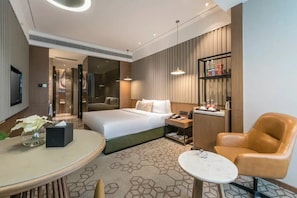A modern hotel room with a bed, bedside table, lamp, chair, and a small table with a vase of flowers.