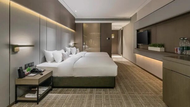 A modern hotel room with a large bed, bedside tables, a TV, and a small kitchenette area. - Guohui Hot Spring Hotel (Fuzhou)