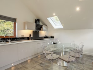 A modern kitchen with a skylight, a dining area with clear chairs, and a view of greenery outside.