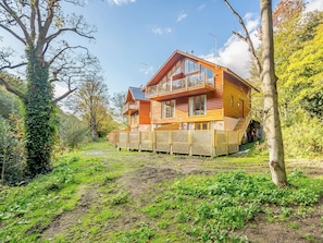 A two-story log cabin with a balcony, surrounded by a wooden fence and lush greenery.