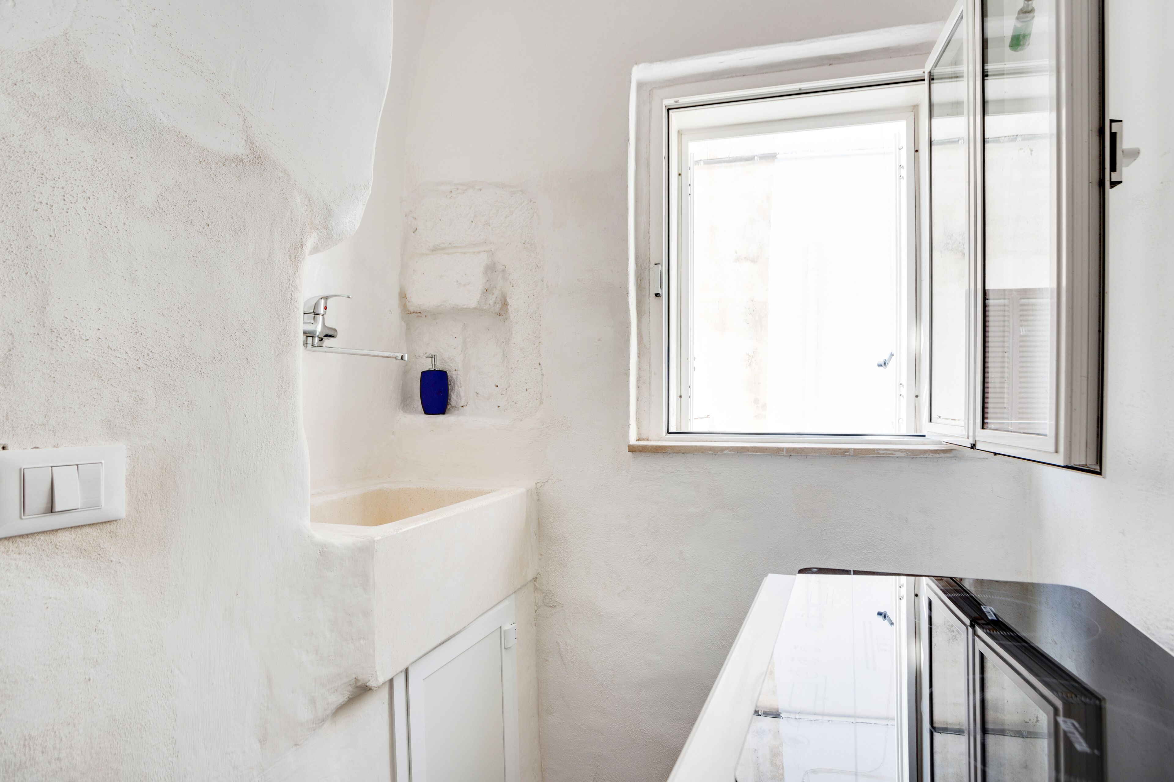 A bathroom with a white sink, a blue soap dispenser, and a window with a view of the outside.