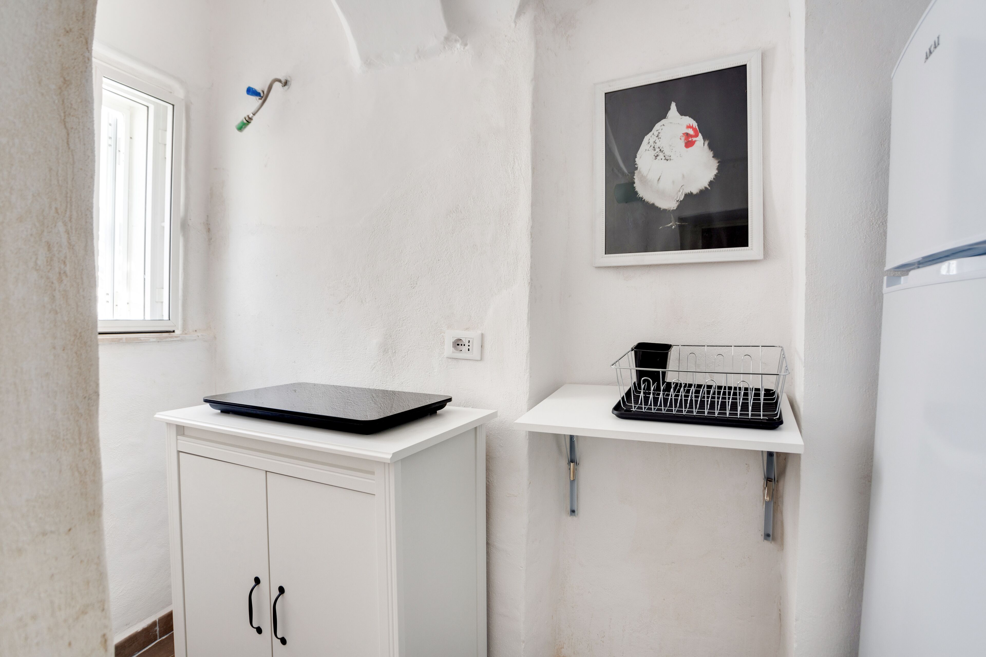 Una cocina blanca con una computadora portátil sobre un mueble, un fregadero y un cuadro en la pared.