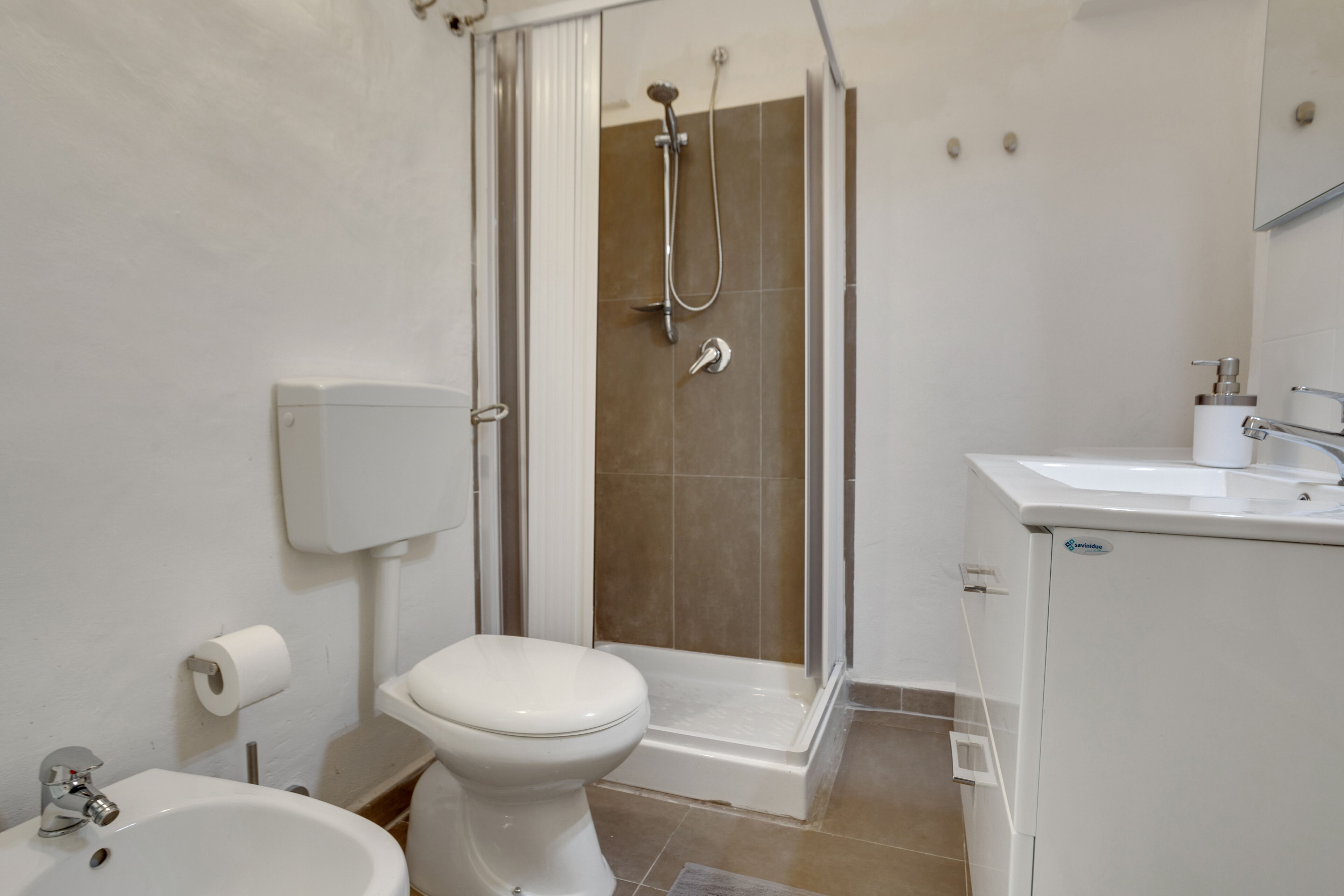 A bathroom with a shower, toilet, sink, and a toilet paper holder.