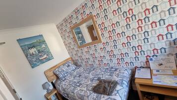 Quarto com cama, cabeceira de madeira, mesa de cabeceira, abajur, quadro emoldurado, mapa e papel de parede estampado.