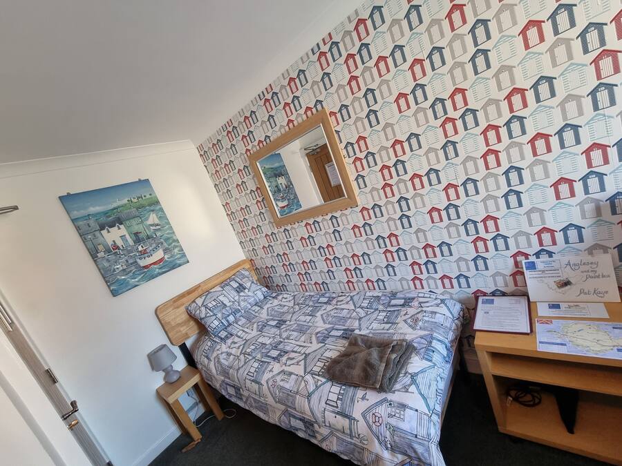 Quarto com cama, cabeceira de madeira, mesa de cabeceira, abajur, quadro emoldurado, mapa e papel de parede estampado.