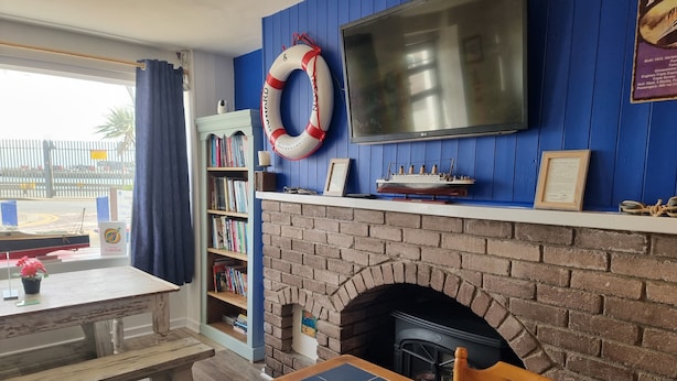A room with a brick fireplace, a bookshelf, a television mounted on a blue wall, and a table with a chair.