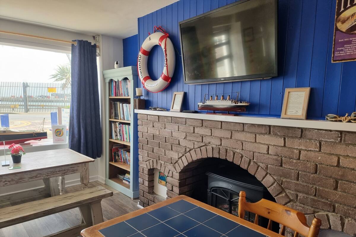A room with a brick fireplace, a bookshelf, a television mounted on a blue wall, and a table with a chair.