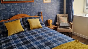 A bedroom with a bed, a chair, a window, and a painting on the wall.