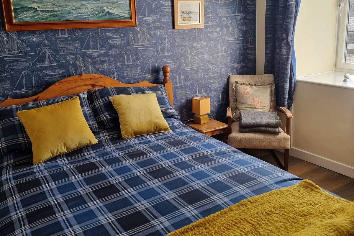 A bedroom with a bed, a chair, a window, and a painting on the wall.