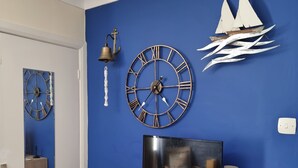 A room with a blue wall, a wooden cabinet with drawers, a television, a clock, and a wall-mounted bell.