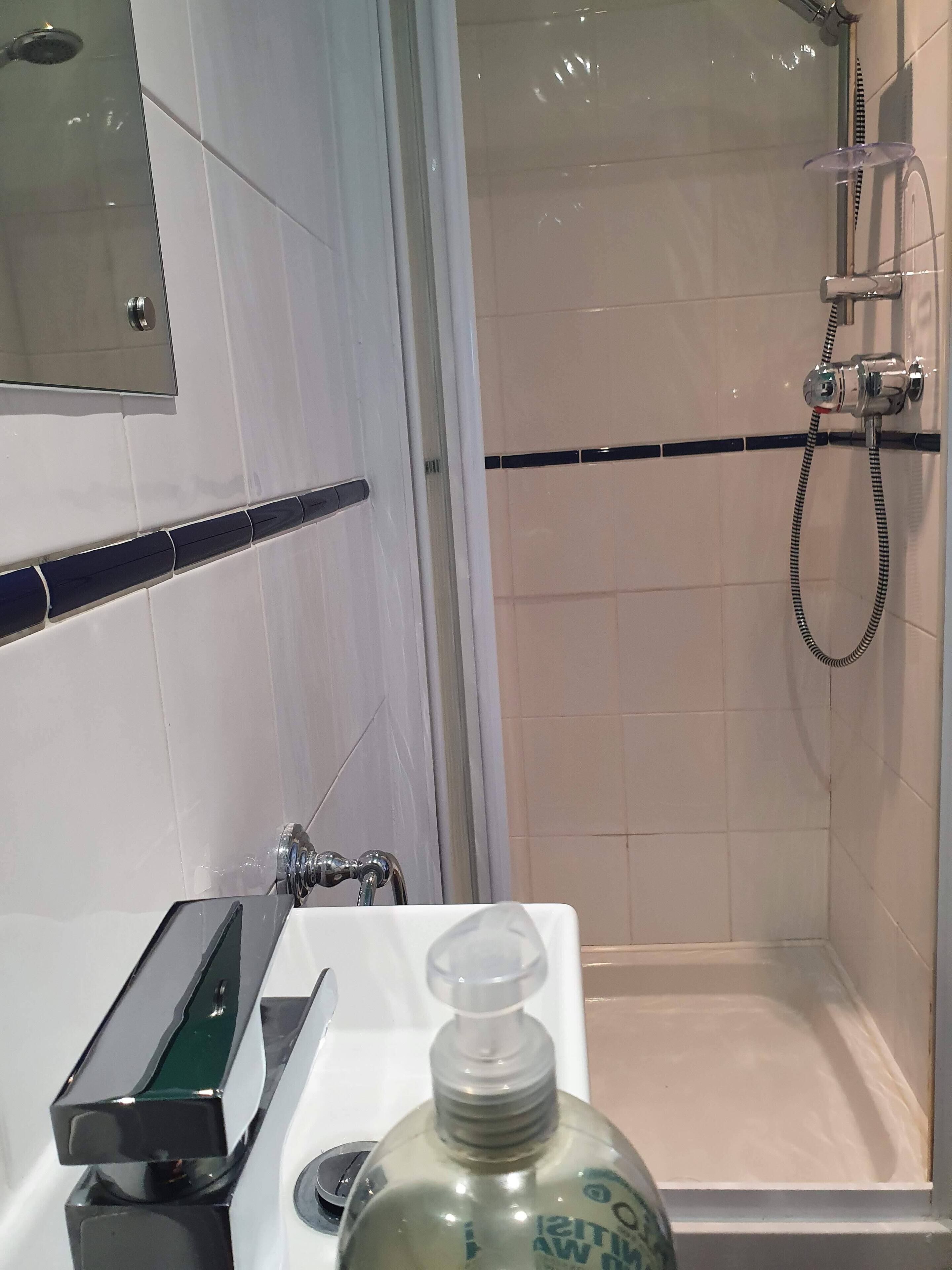 A bathroom with a shower, a mirror, and a soap dispenser on the sink.