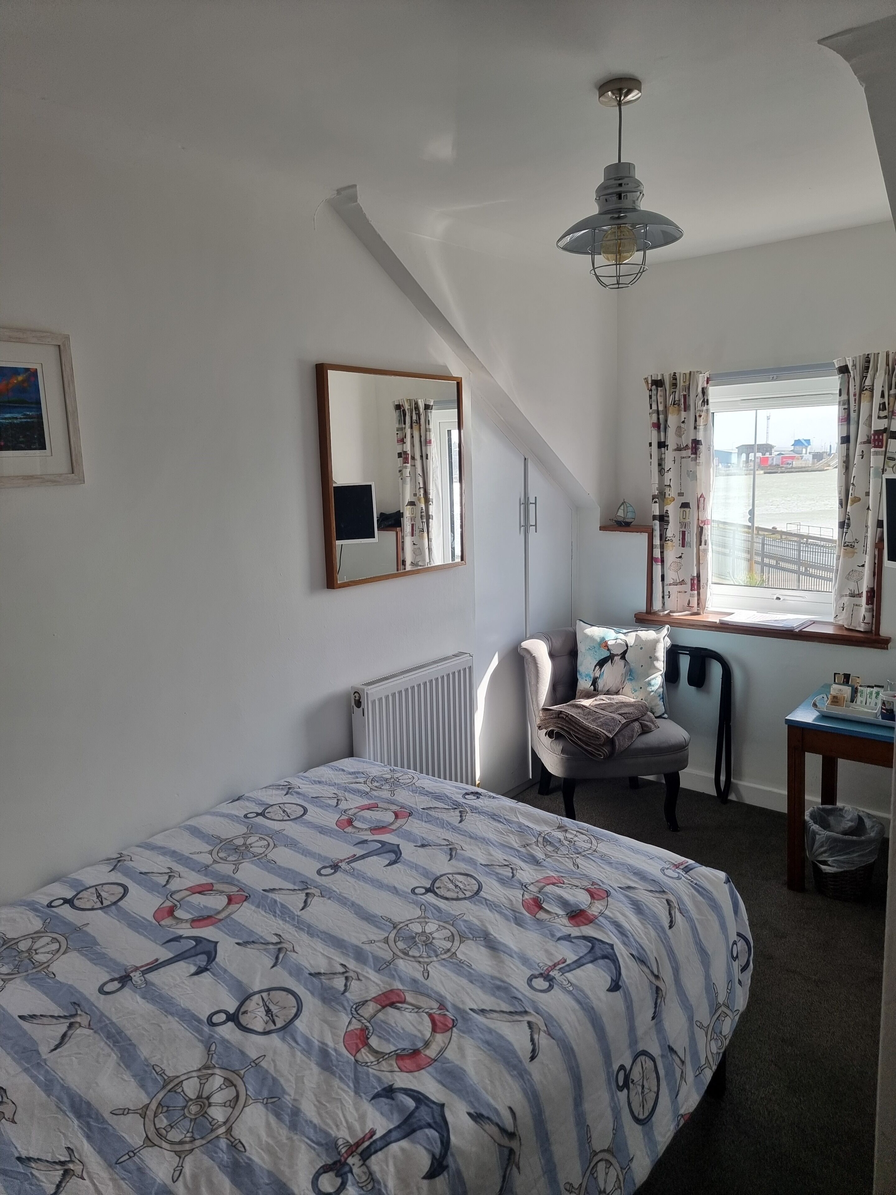 Une chambre à coucher comprenant un lit, une chaise, un bureau, un radiateur, une fenêtre avec des rideaux, un miroir et un luminaire au plafond.