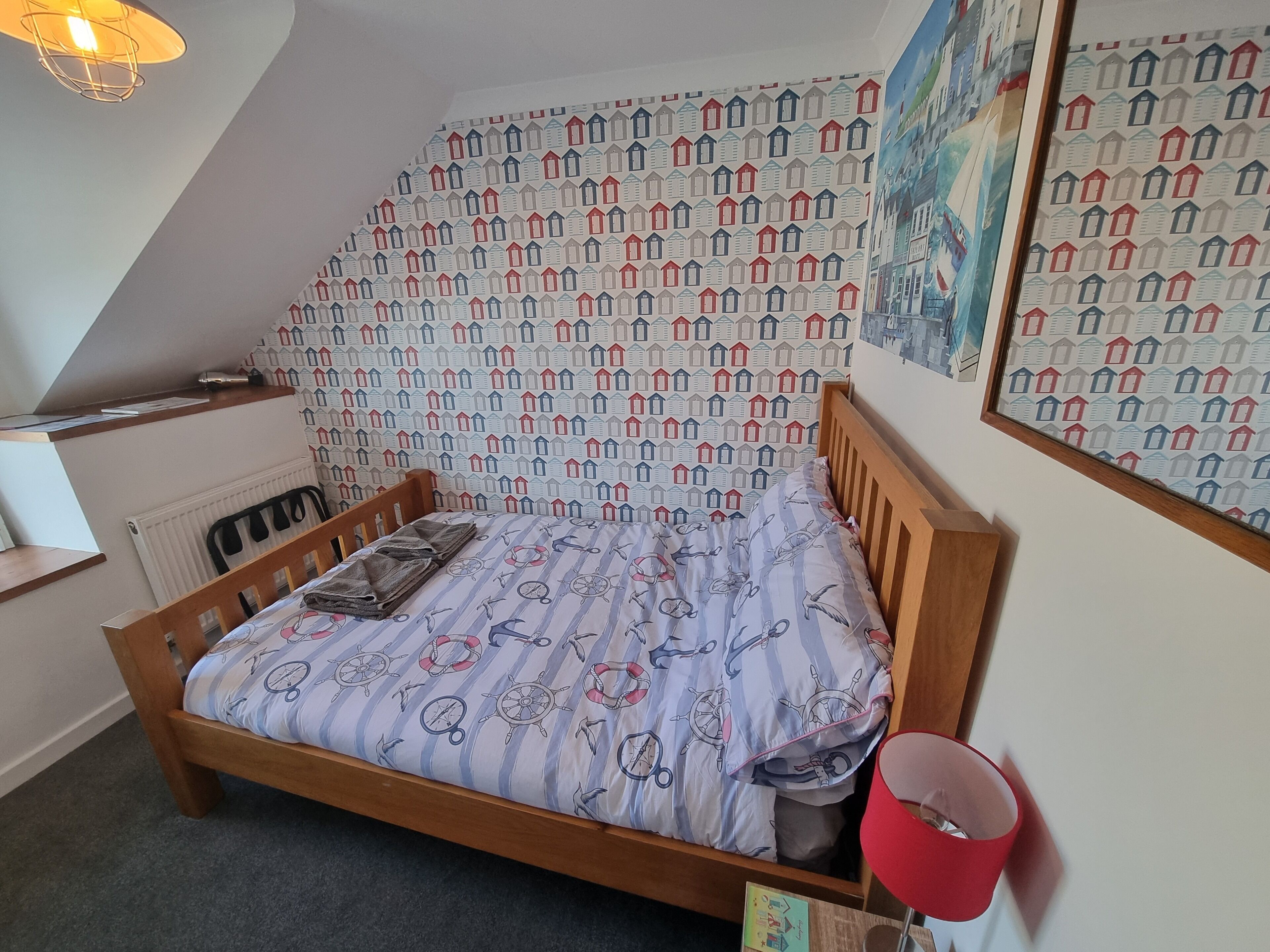 A bedroom with a wooden bed, a radiator, a red lamp, and patterned wallpaper.