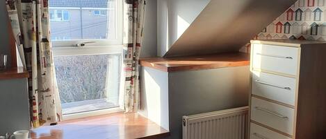 Une chambre avec une fenêtre, un lit, une commode et un radiateur.