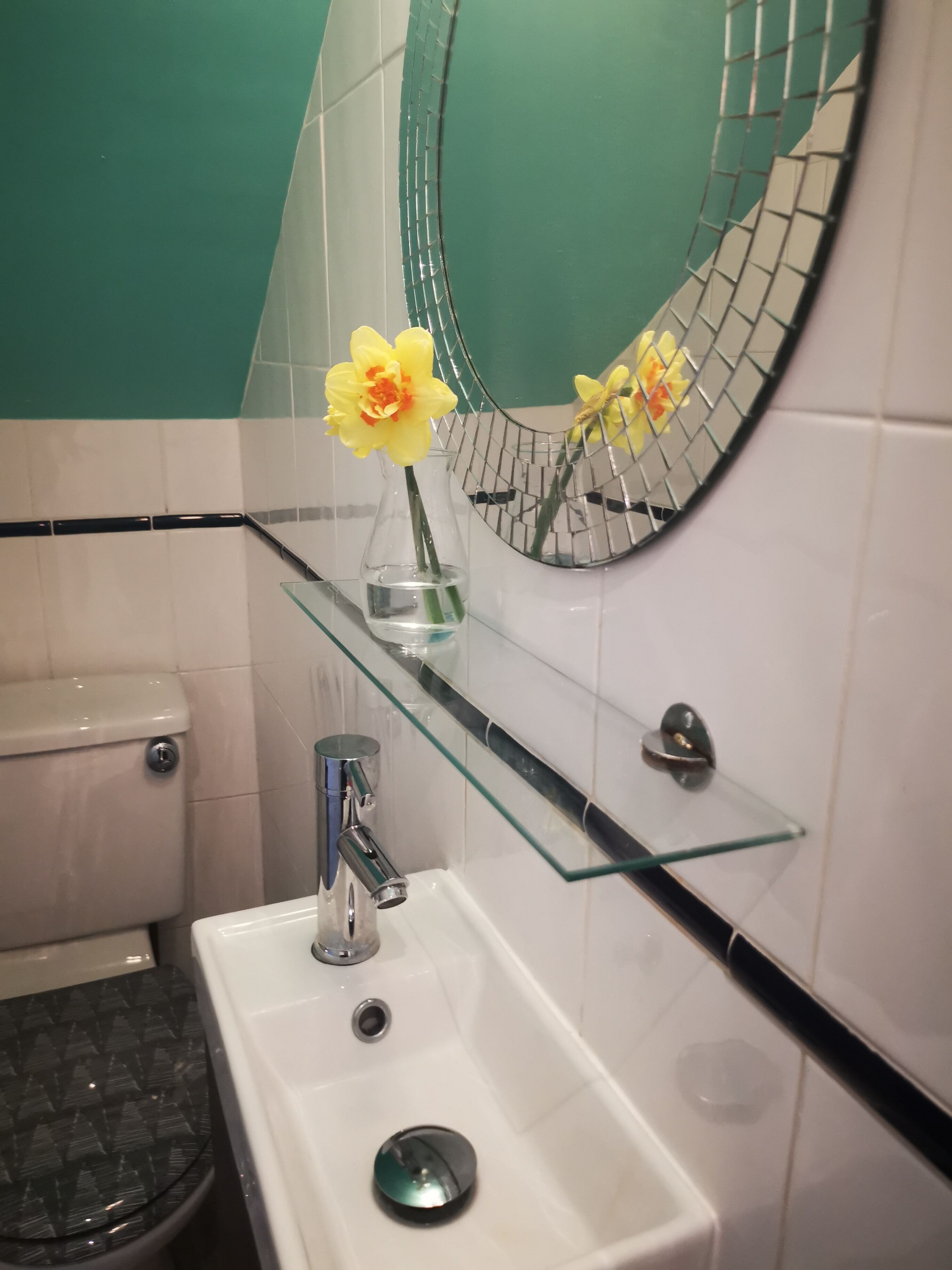 Un baño con repisa de vidrio, espejo redondo, lavabo blanco y retrete.