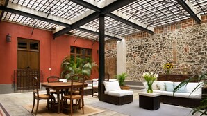 Un'ampia area interna con soffitto alto, parete in pietra e tavolo in legno con sedie.