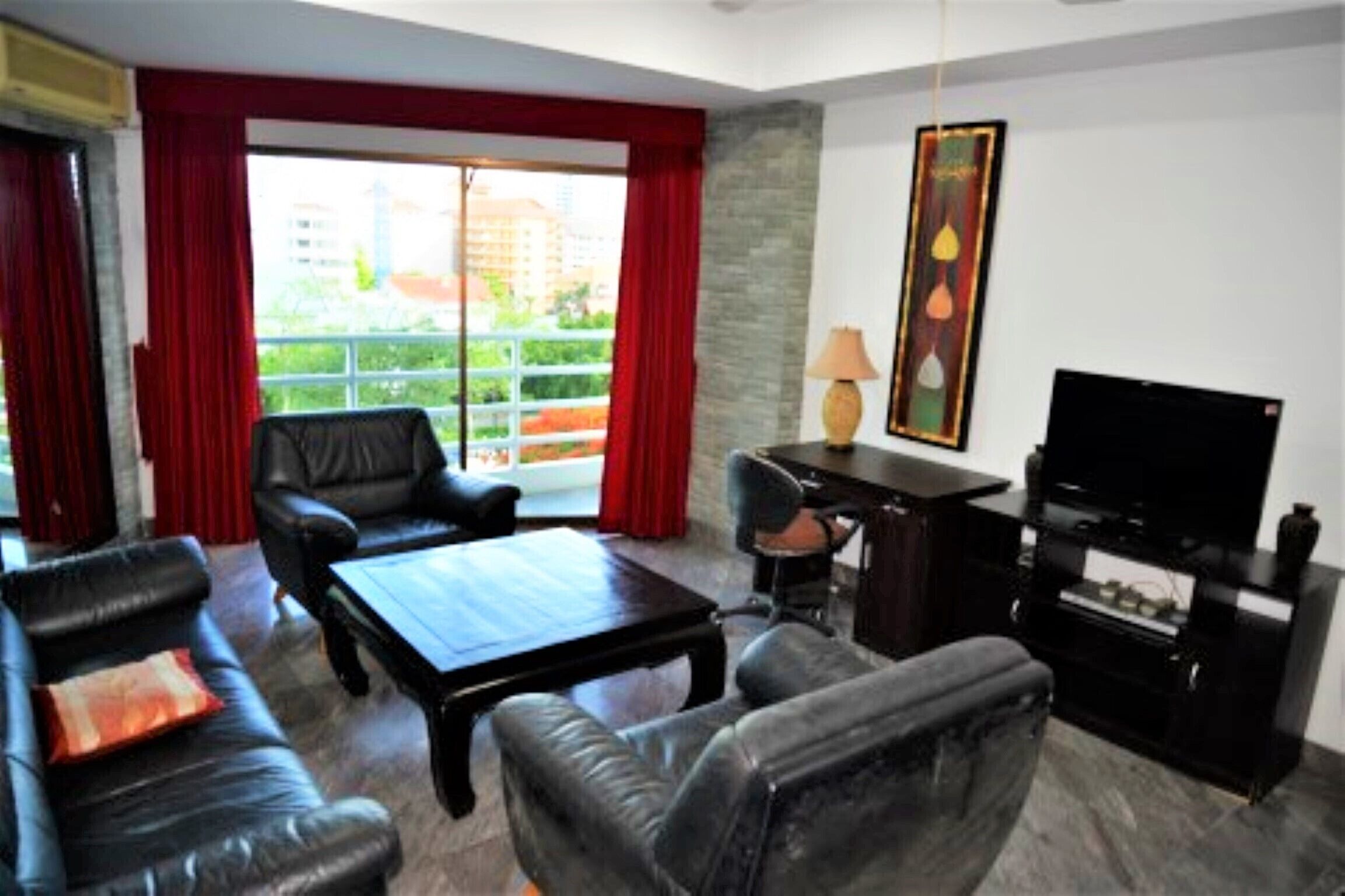 Un salon comprenant un canapé, des fauteuils, une table basse, un téléviseur et un balcon avec des rideaux rouges.