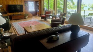Una sala de estar acogedora con televisor, paredes de madera, una estantería y vistas al exterior.