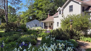 Una casa con porche, rodeada por un jardín lleno de plantas y flores.