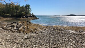Una costa rocosa con vista despejada al mar, una pequeña isla en la distancia y un área boscosa con árboles.