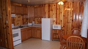 Une cuisine compacte avec un lambris en bois, des appareils électroménagers blancs et un coin repas avec des chaises en bois.