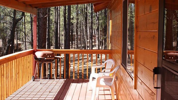 Une terrasse en bois avec une rambarde, deux chaises et une table.