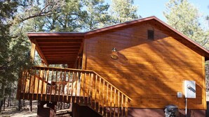 A wooden cabin with a wooden staircase leading to a deck, surrounded by trees. - Whispering Pines - Cabin 31 (Spa Tub) (Pinetop)