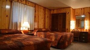 Une pièce aux murs lambrés, comprenant deux lits, un bureau, une chaise et un miroir avec éclairage intégré.