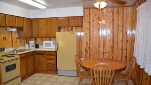 Une cuisine avec des meubles de rangement en bois, un réfrigérateur jaune, un four à micro-ondes, une cuisinière et une table à manger avec des chaises.