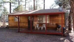 A small wooden cabin with a porch, two chairs, and a chimney. - Whispering Pines Resort-Cabin #18 (Pinetop)