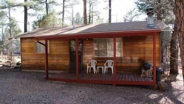 Une petite cabane en bois avec une véranda, deux chaises et une cheminée.