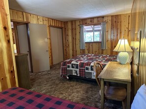 Une chambre à coucher avec un lit, une chaise, une table, une lampe et une fenêtre avec des rideaux.