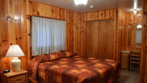 Une chambre à coucher aux murs lambrissés, avec un lit, une table de chevet avec une lampe, une fenêtre avec des rideaux et un miroir.