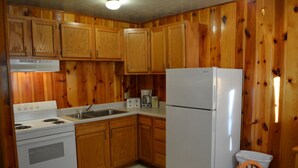 Une cuisine avec des meubles de rangement en bois, une cuisinière blanche, un évier, un réfrigérateur et une machine à café.