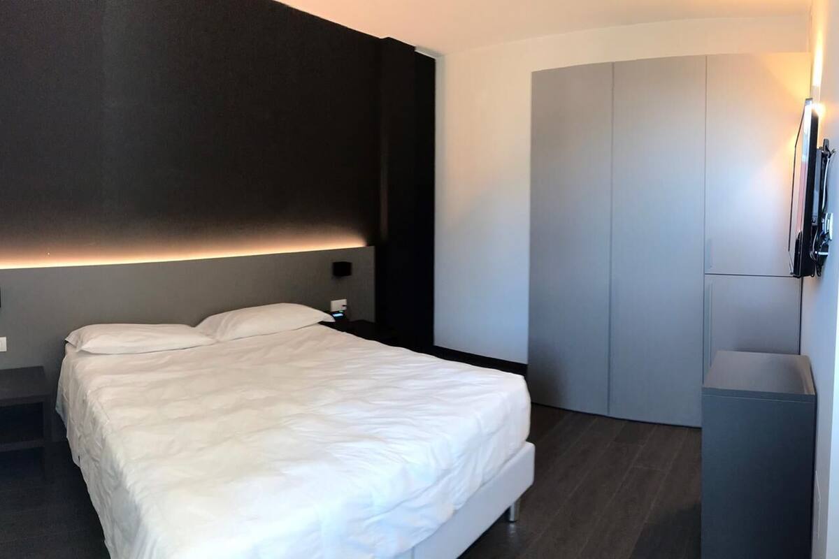 A modern hotel room with a large bed, a wardrobe, and a small bedside table.