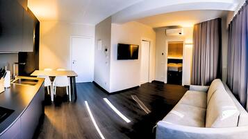 Una sala de estar moderna con un sofá, un televisor montado en la pared y una cocina con una mesa de comedor y sillas.