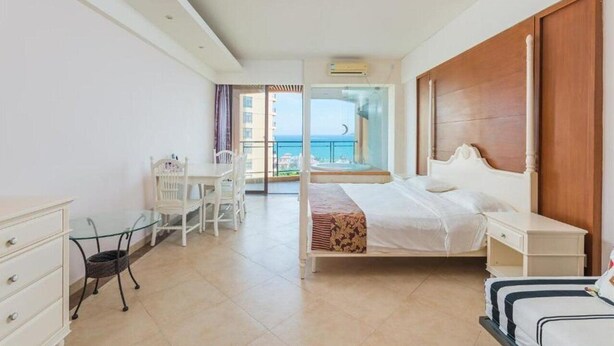 Une chambre d’hôtel avec un lit, un bureau et une chaise. Elle dispose d’un balcon avec vue sur la mer.