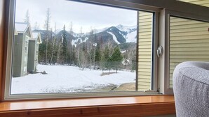 Une pièce dotée d’une grande fenêtre donnant sur un paysage enneigé, avec des montagnes et des arbres.