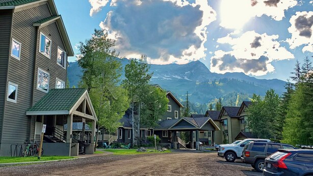 Un quartier résidentiel avec des maisons, un chemin de terre, des voitures garées et des montagnes en arrière-plan.