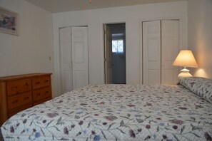 A bedroom with a floral bedspread, a wooden dresser, and a lamp. - Whispering Pines - Victorian House (Pinetop)
