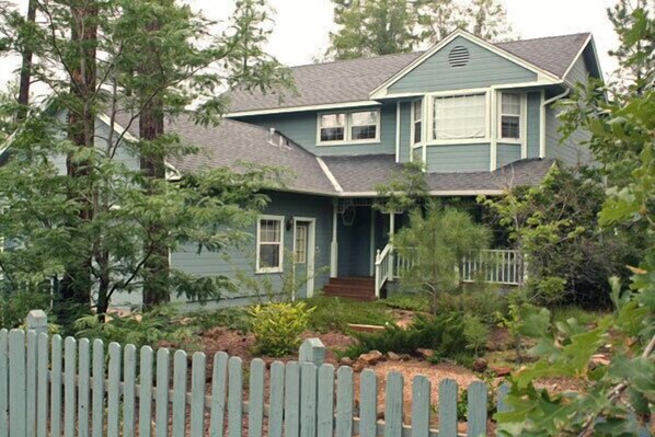 A two-story house with a front porch, surrounded by trees and a wooden fence. - Whispering Pines - Victorian House (Pinetop)