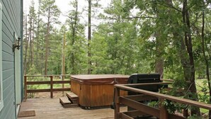 Una terraza de madera con un jacuzzi y una parrilla, rodeada de árboles.
