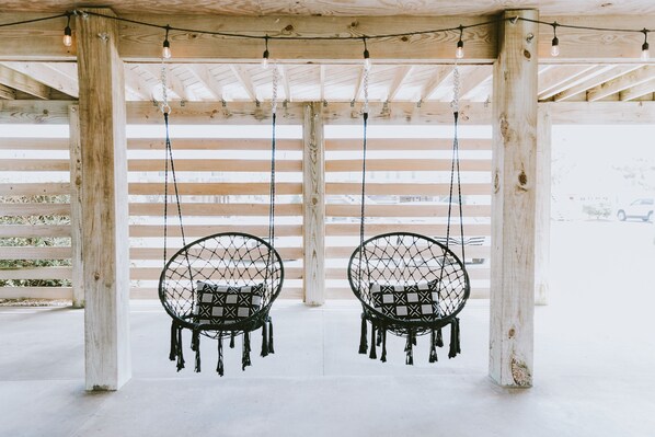 Two black swing chairs hanging from a wooden pergola with string lights.
