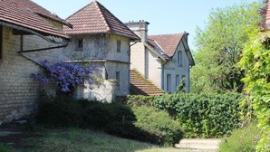 En traditionel bygning i sten med et tegltag, omgivet af frodig vegetation og en klar himmel.