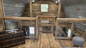 L’intérieur d’un chalet rustique, avec un plancher en bois, un téléviseur posé sur une commode et une petite fenêtre.