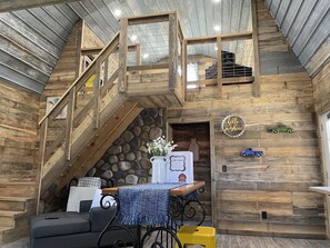 A rustic interior with a wooden staircase, a stone wall, a table with a blue tablecloth, and a sign that says 'Hello Sunshine'. - The Little Barn on the Hill...NEW! min. from town. Great back porch view w/ Loft (Mountain View)