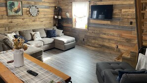 Un salon chaleureux avec des boiseries, un canapé d’angle, une table basse agrémentée d’un set de table et un téléviseur à écran plat fixé au mur.
