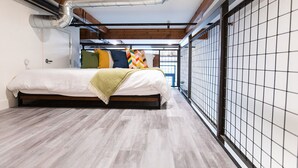 Un dormitorio con cama, piso de madera, ventana y pared con celosía metálica.