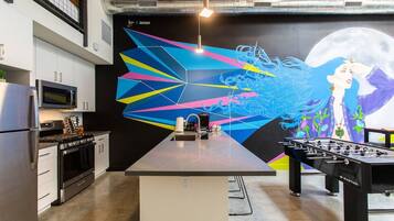 A modern kitchen with a central island, a foosball table, and a large abstract mural on the wall.