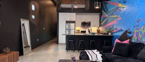 Une cuisine moderne dotée d’un îlot central, de tabourets de bar et d’une fresque murale abstraite aux couleurs vives.